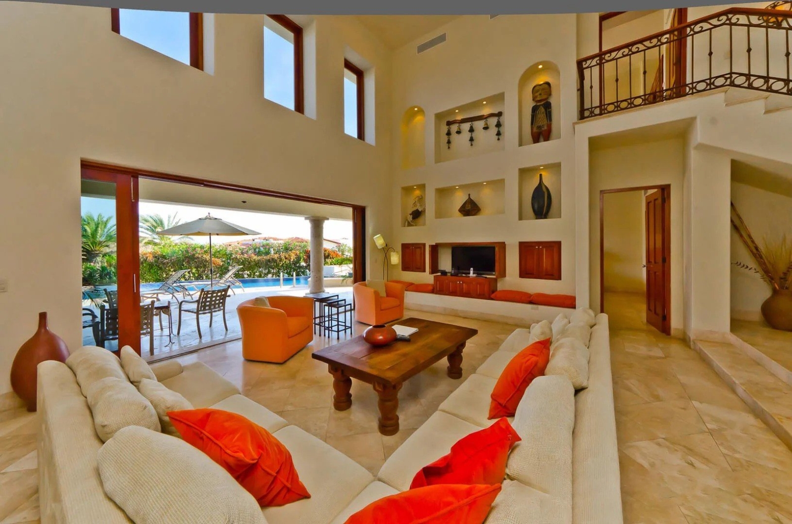 Bright living space in Los Cabos villa with cozy sectional seating, wall niches with decor, and sliding doors opening to private pool area
