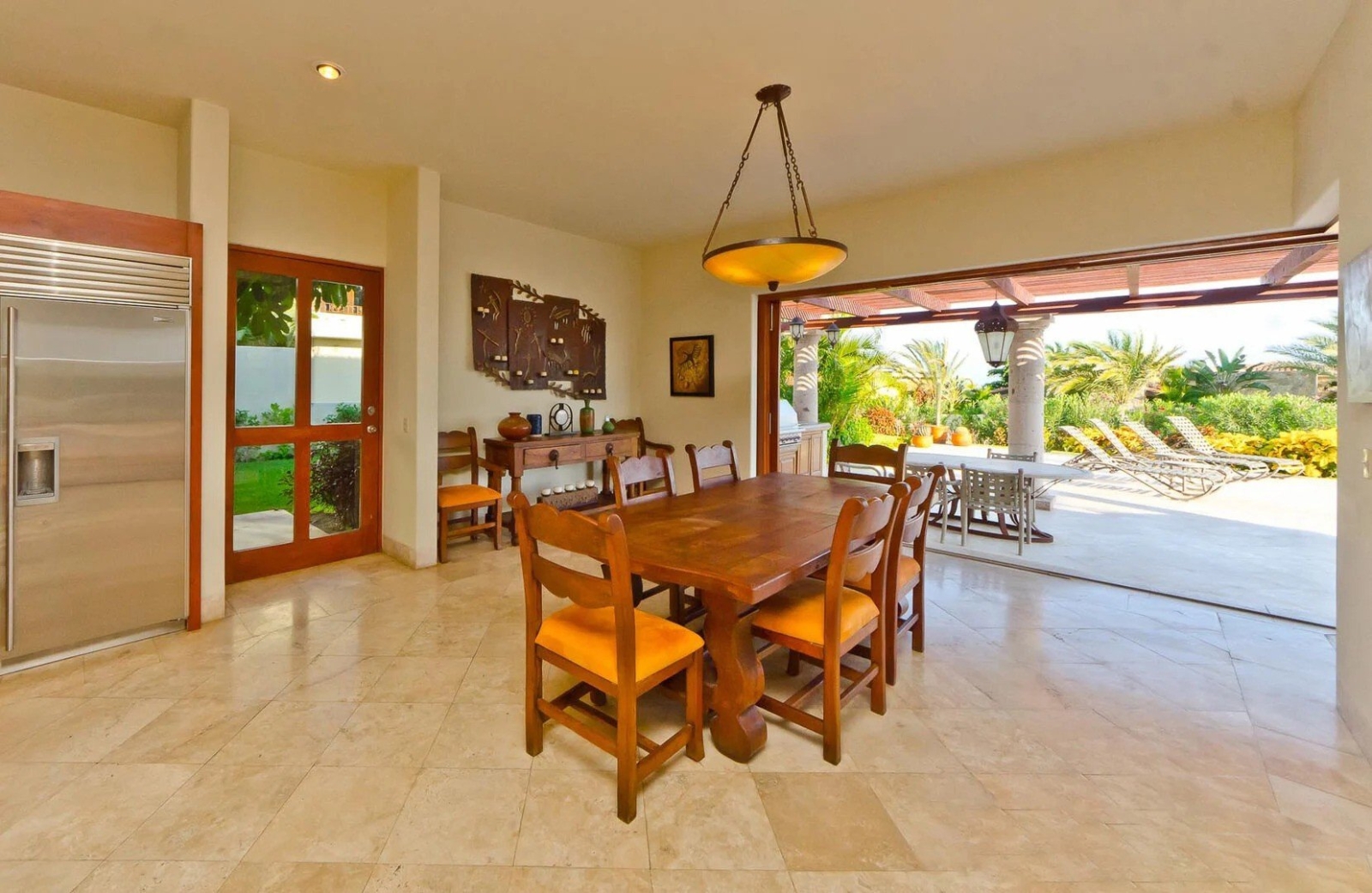 Indoor-outdoor dining area of a luxury Los Cabos villa with wood dining table, patio lounge chairs, and garden views