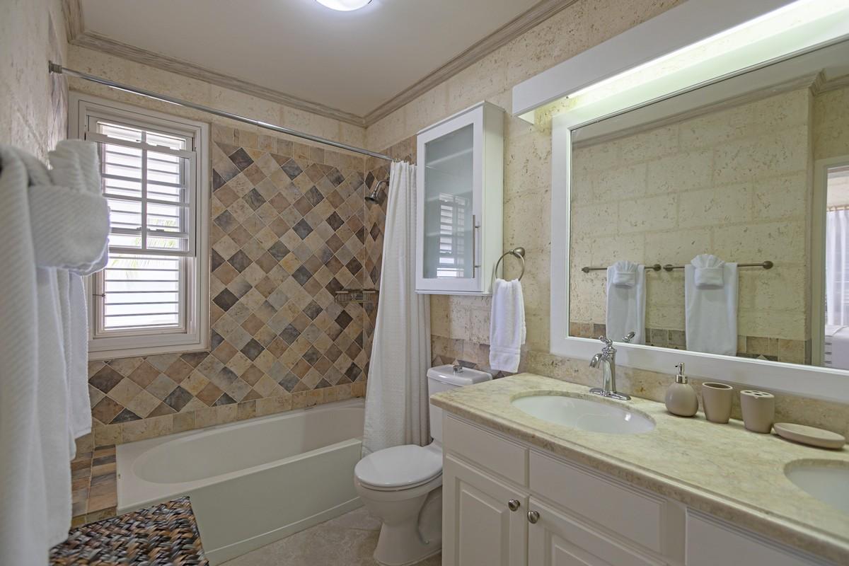 Bright bathroom in a Barbados villa featuring a tub-shower combo, coastal tilework, and ample natural light