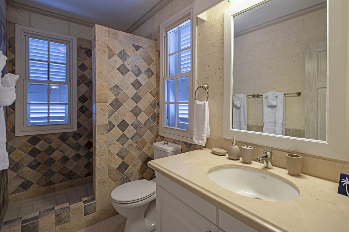 Elegant walk-in shower bathroom in a Barbados villa with diamond-patterned tiles and bright vanity lighting