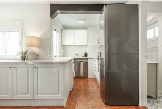 Modern white kitchen with stainless steel appliances and traditional tile floors, fully equipped for guests staying in Malaga with Charity Ace’s Spain for 4 experience.