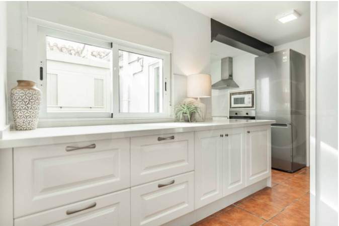 Bright and modern kitchen with sleek white cabinetry, large windows, and stainless steel appliances—part of the stylish Malaga apartment in the Charity Ace Spain for 4 travel package.