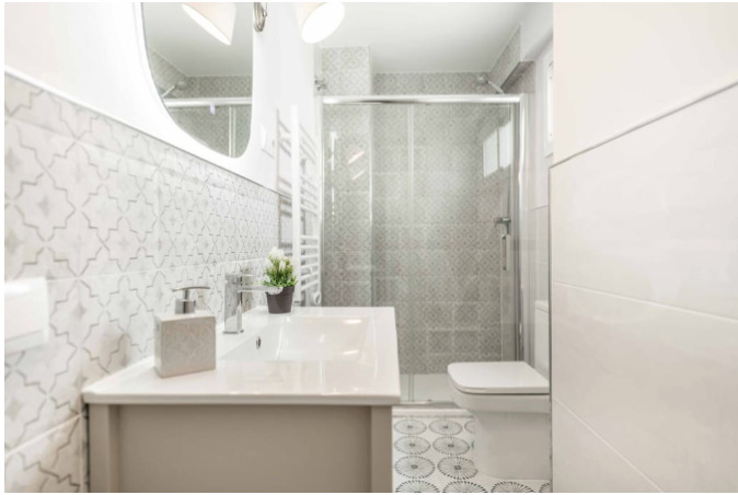 Elegant bathroom with patterned Spanish tiles, walk-in glass shower, and contemporary sink—highlighting the boutique comfort of the Malaga stay included in Charity Ace's Spain experience for 4.