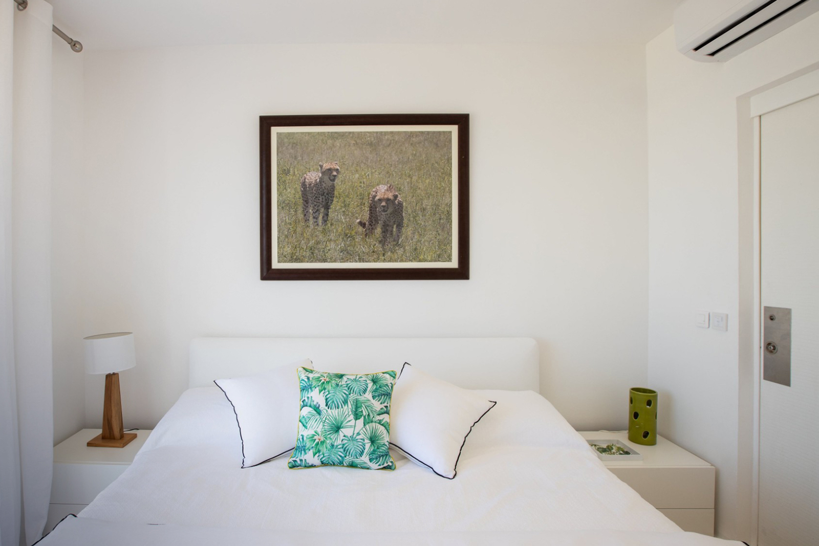 Minimalist bedroom in St. Martin with crisp white linens, tropical-themed pillows, and framed wildlife art, blending simplicity and island charm.