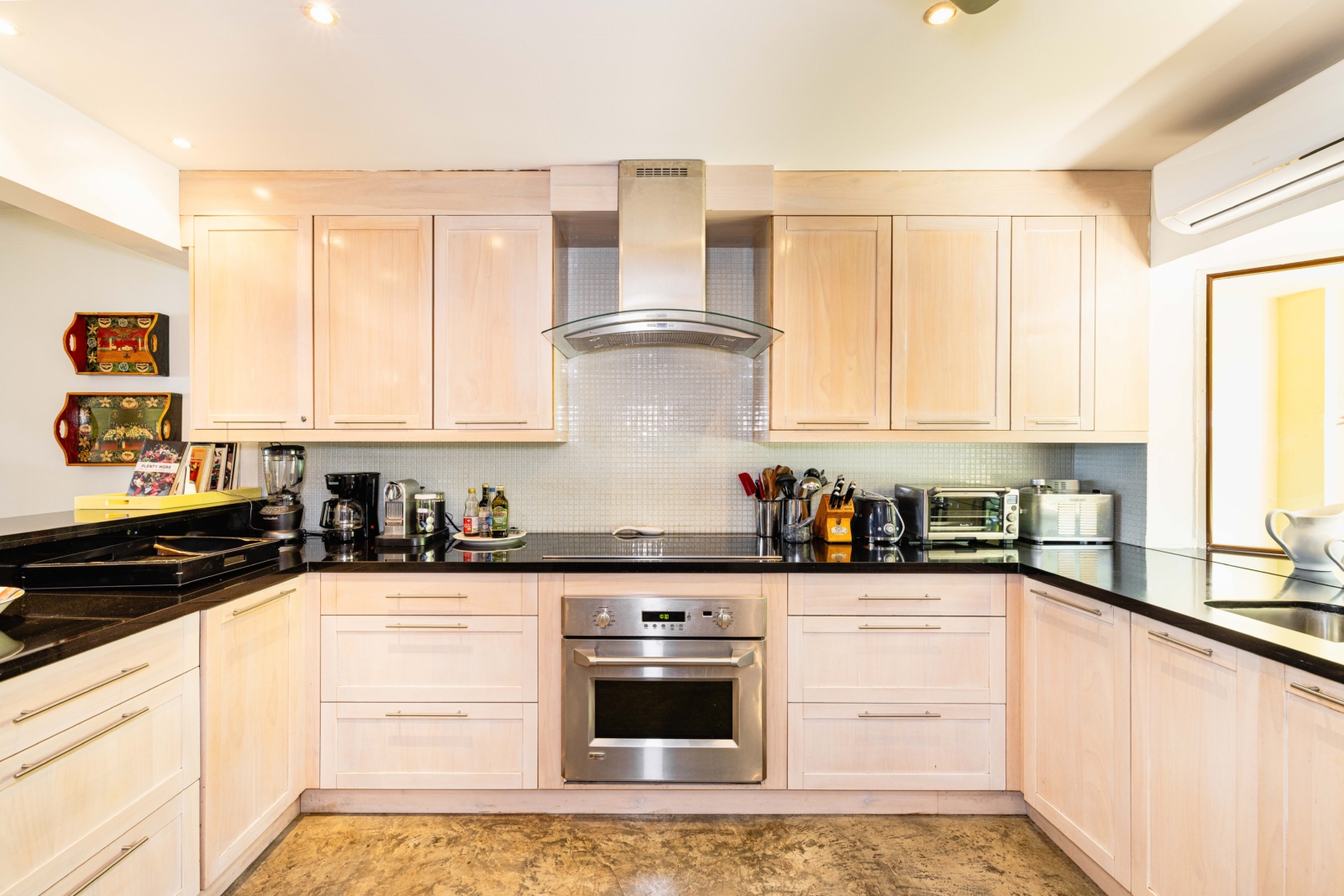 Contemporary kitchen with light wood cabinetry, stainless steel appliances, and black countertops – Charity Ace Costa Rica villa