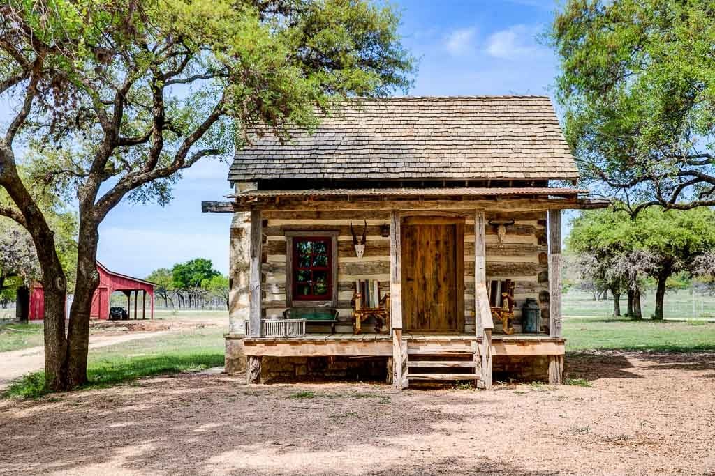 Charming rustic log cabin with wooden porch surrounded by Texas countryside and oak trees