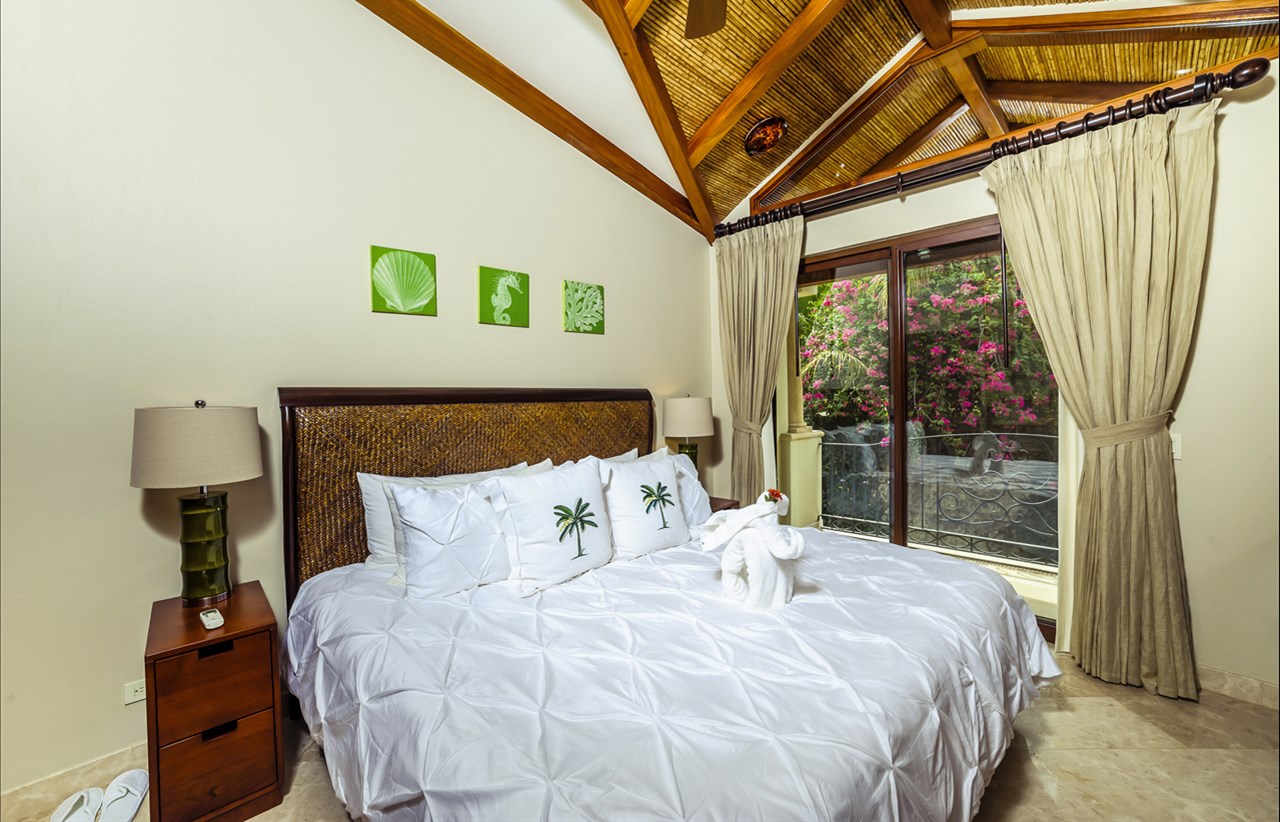 Tropical-style bedroom with vaulted ceiling, palm-themed pillows, and garden views in Costa Rica villa – Charity Ace luxury getaway