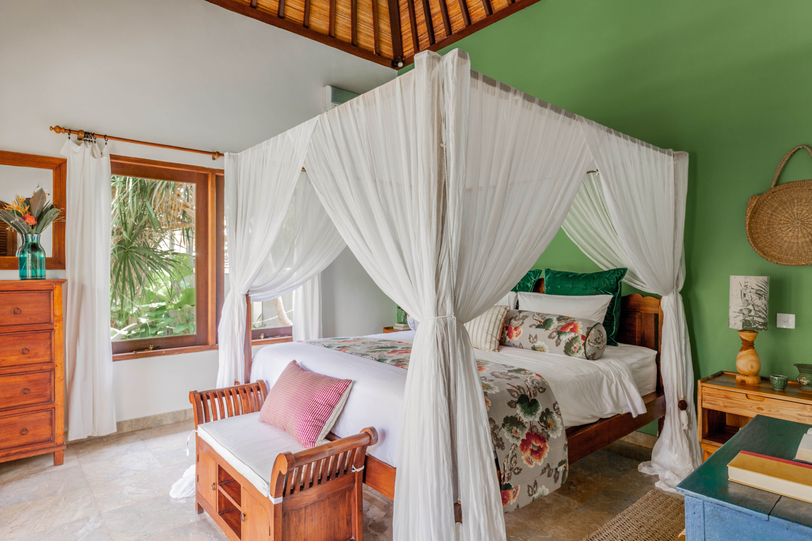 A beautifully decorated bedroom featuring a four-poster canopy bed with floral linens, green accent wall, and wooden furnishings, offering a serene retreat in Bali.