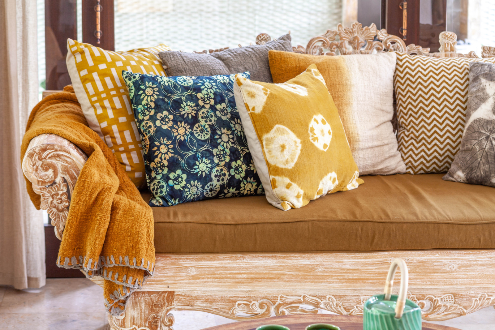A cozy carved wooden sofa adorned with bright, patterned cushions and throws, enhancing the warm and inviting atmosphere of a tropical retreat.