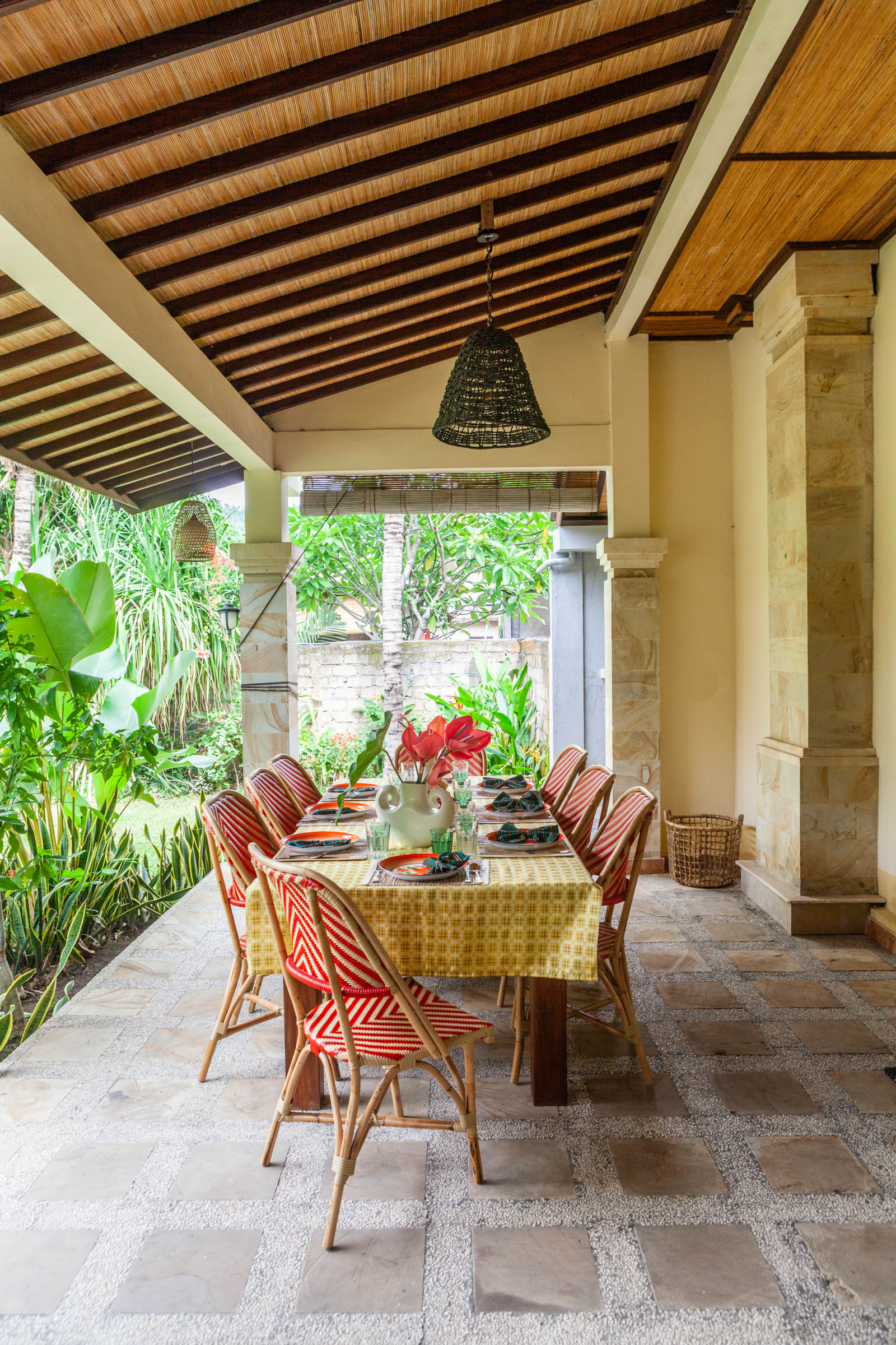 A tropical alfresco dining table set for a gathering, with colorful chairs and lush greenery creating an inviting outdoor experience.