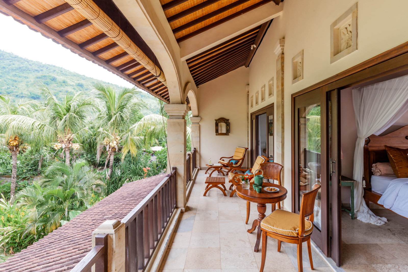 Bright and airy bedroom with a canopy bed and a private balcony overlooking lush greenery in Bali.