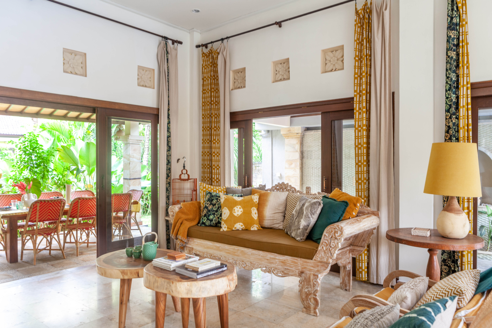 Spacious living room with natural light, traditional carved furniture, and vibrant cushions in a Bali villa.